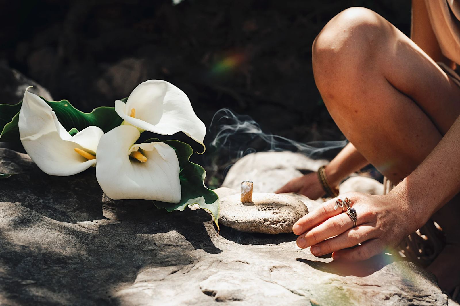 Hands placing incense beside white calla lilies on stone